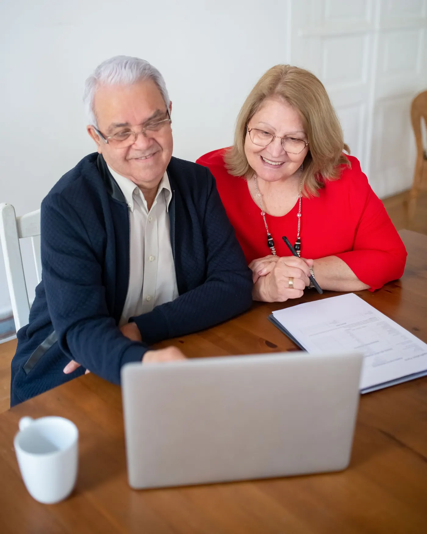 An older couple smiling at a laptop at their dining table